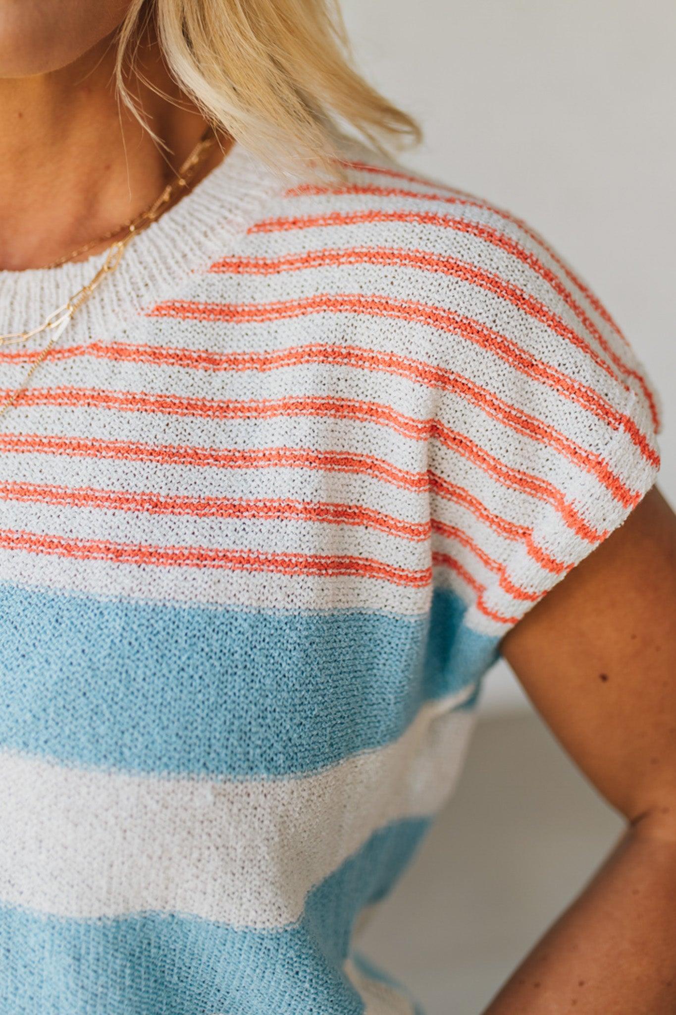 BLONDE WOMAN WEARING A STRIPED LIGHTWEIGHT SLEEVELESS DROP SHOULDER SUMMER SWEATER TOP IN RED WHITE AND BLUE.