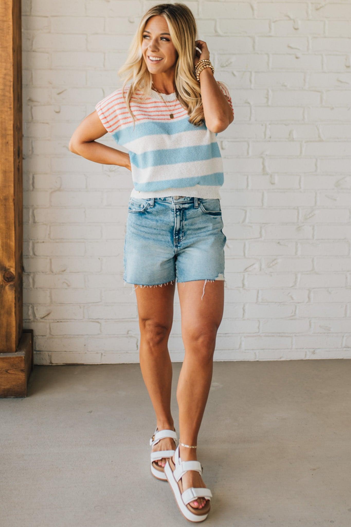 BLONDE WOMAN WEARING A STRIPED LIGHTWEIGHT SLEEVELESS DROP SHOULDER SUMMER SWEATER TOP IN RED WHITE AND BLUE.
