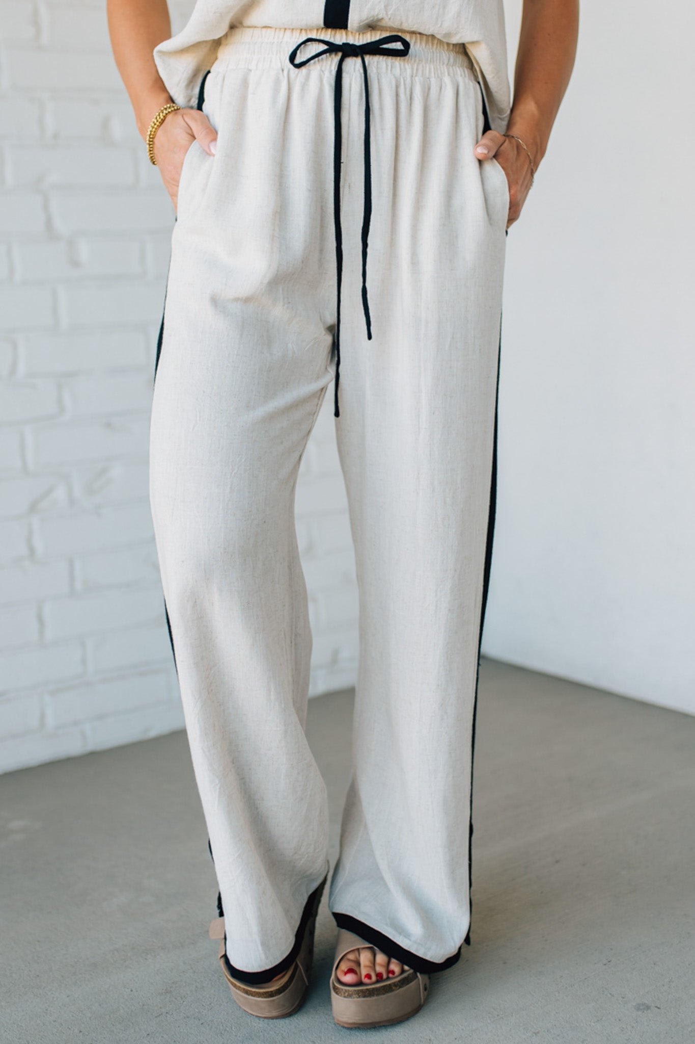 Person wearing white pants with black stripes against a white brick wall.