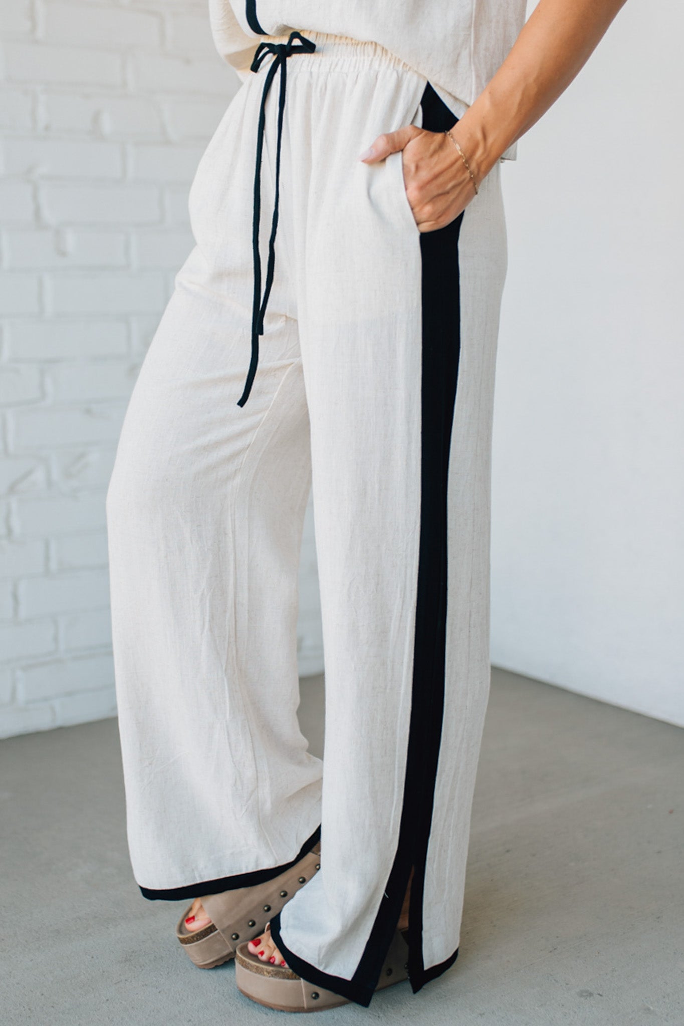 White pants with black trim worn by a person against a white brick wall.