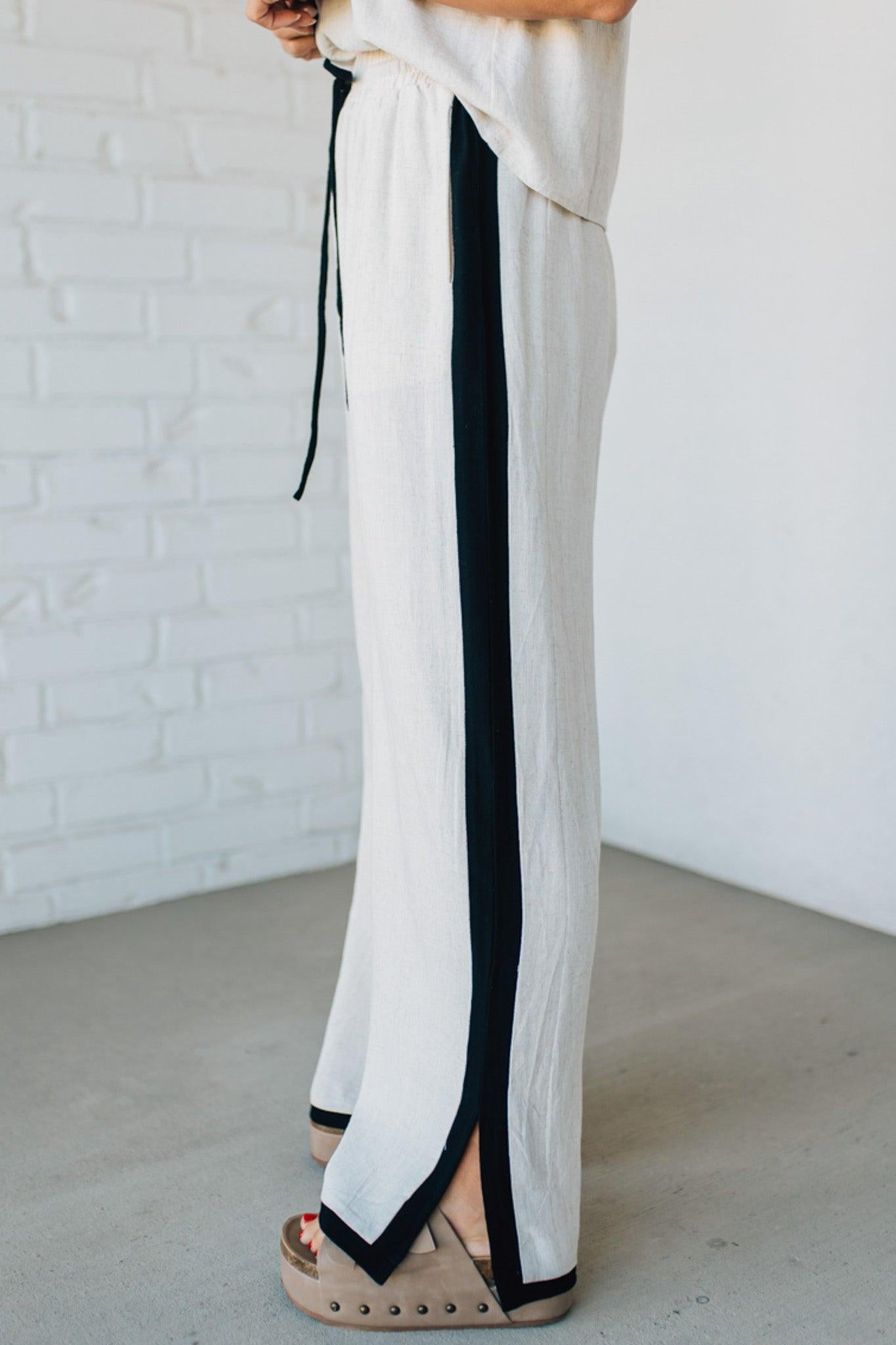 White pants with black stripes worn by a person against a white brick wall.