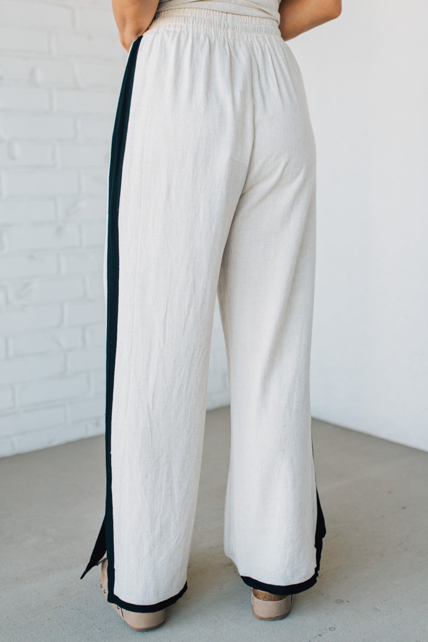 White pants with black trim worn by a person against a white brick wall.