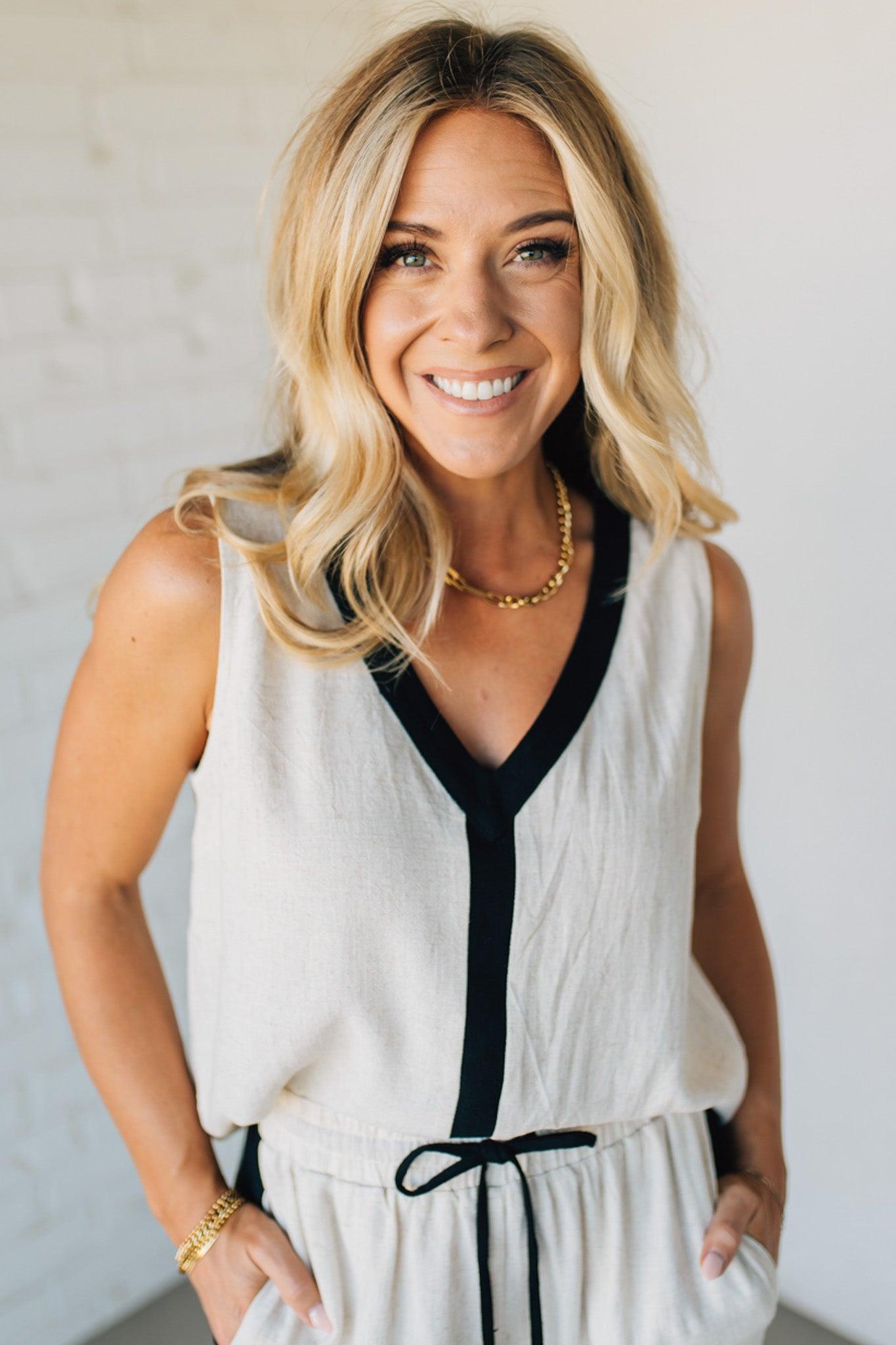 Woman wearing a white sleeveless dress with black trim against a light background