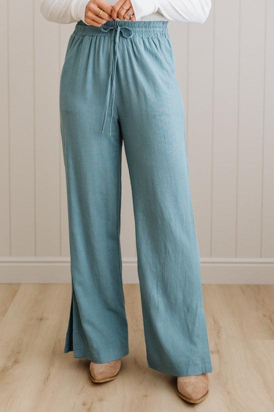 Person wearing teal wide-leg pants with a white top against a neutral background