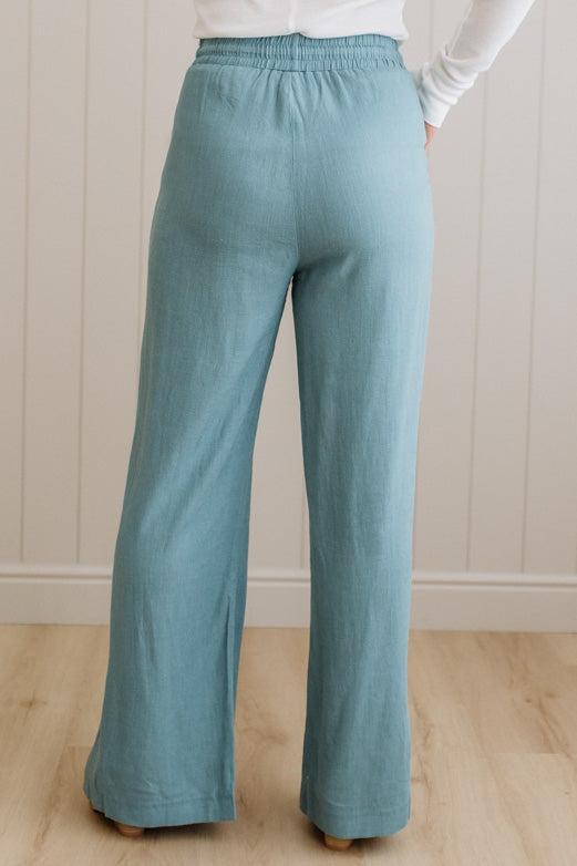 Teal pants worn by a person against a white paneled wall.