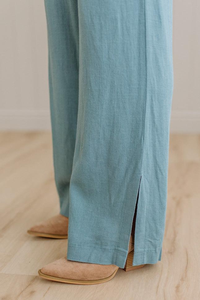 Teal pants with a split design worn by a person on a wooden floor.