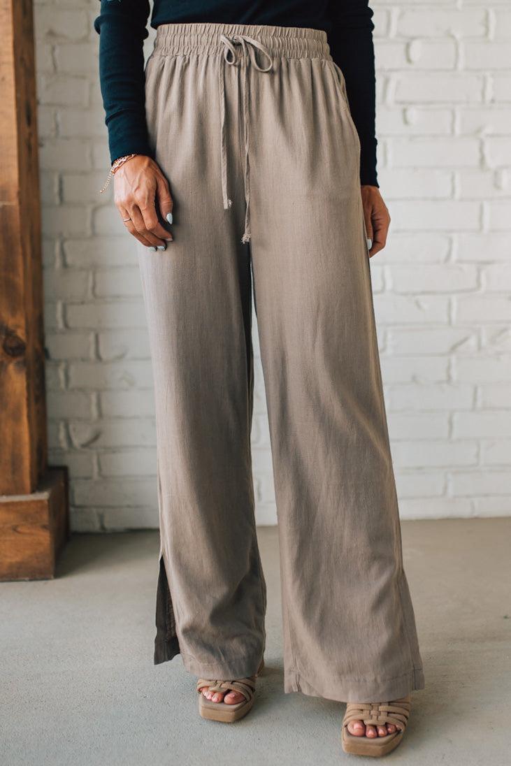 Beige wide-leg pants worn by a person against a white brick wall.