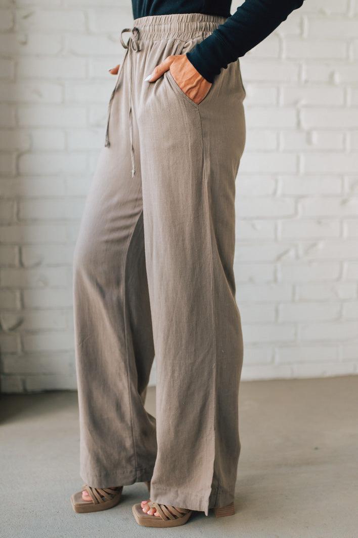 Person wearing beige wide-leg pants against a white brick wall.