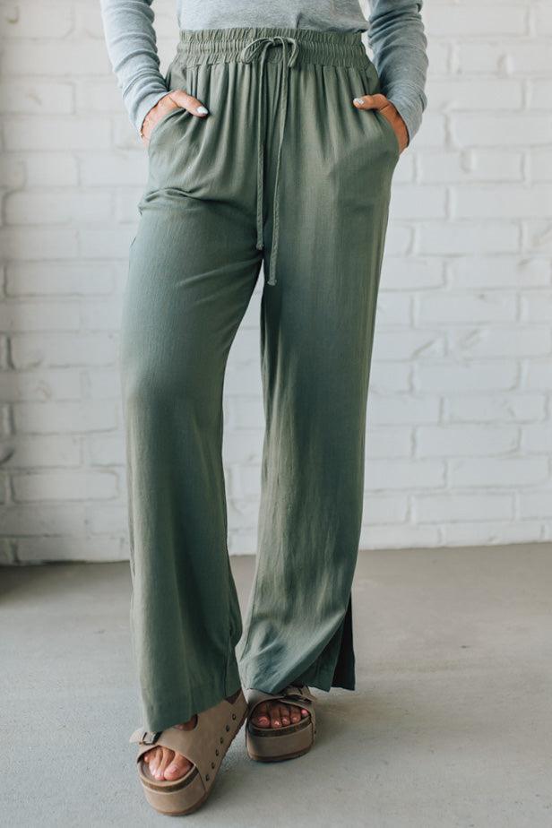 Person wearing green wide-leg pants with a white brick wall background
