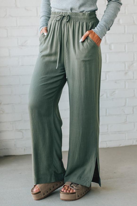Person wearing green wide-leg pants with a white brick wall background