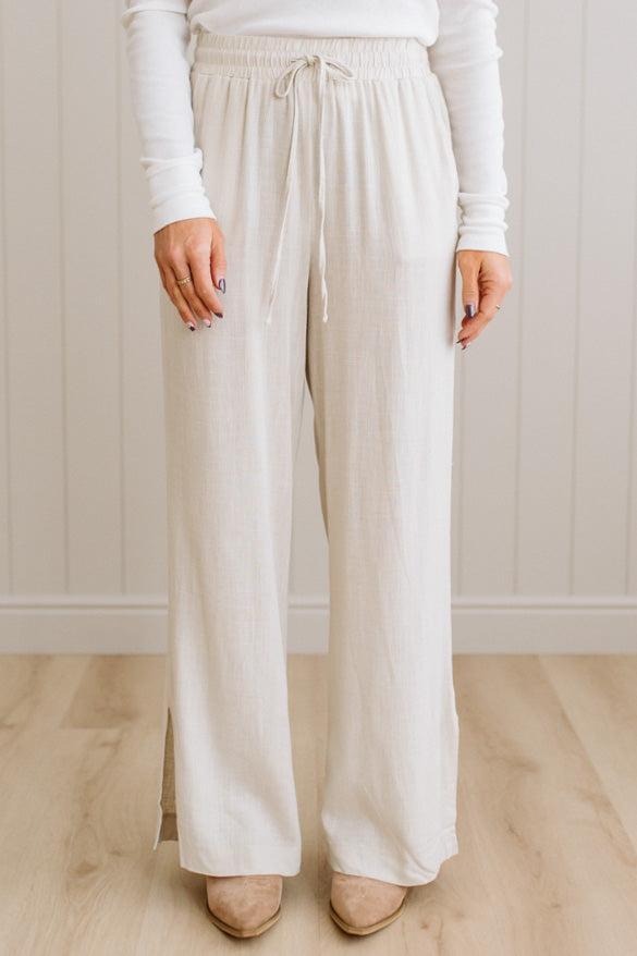 Person wearing beige pants and a white long-sleeve shirt against a plain background