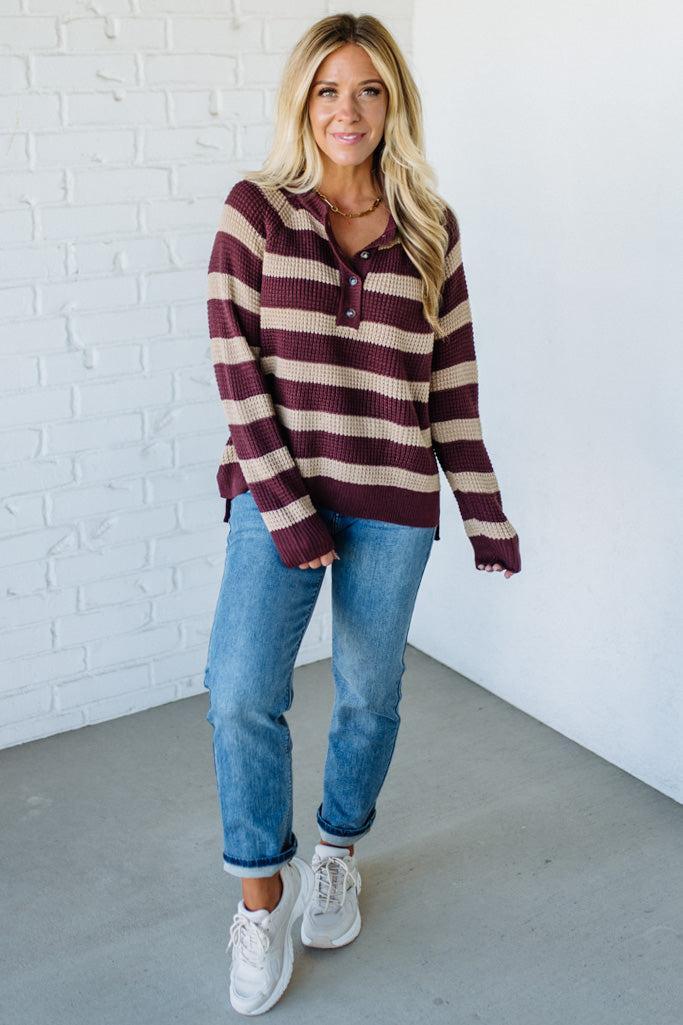 Woman wearing a striped sweater and jeans against a white brick wall.