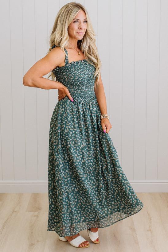 Woman wearing a green floral dress against a white paneled wall.