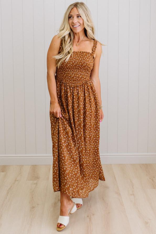 Woman wearing a brown polka dot dress standing against a white paneled wall.