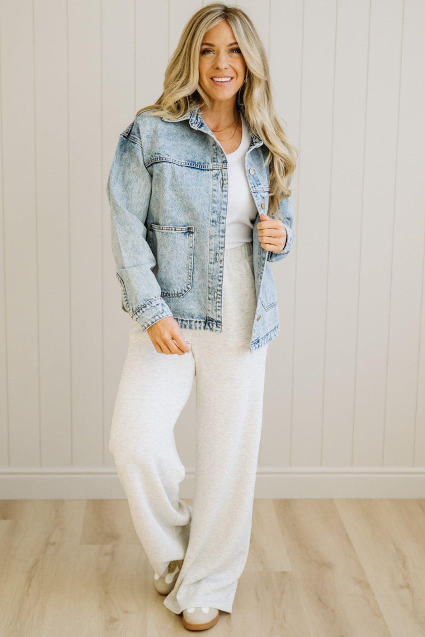 Woman wearing a denim jacket over a white top and pants in a neutral setting