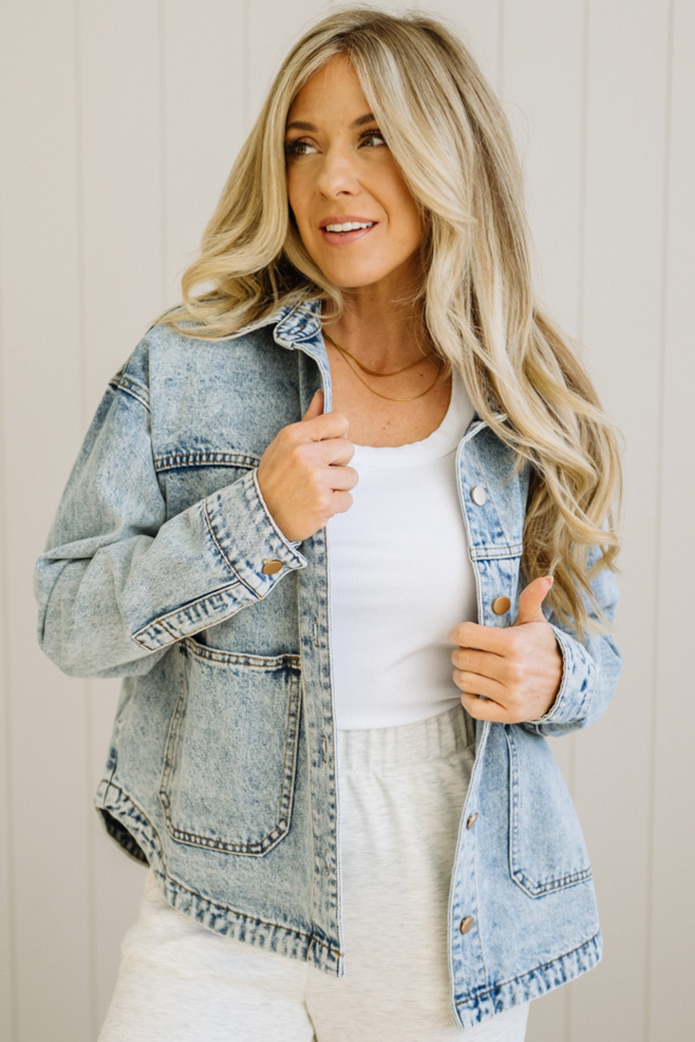 Woman wearing a denim jacket over a white top and pants, standing against a plain background.
