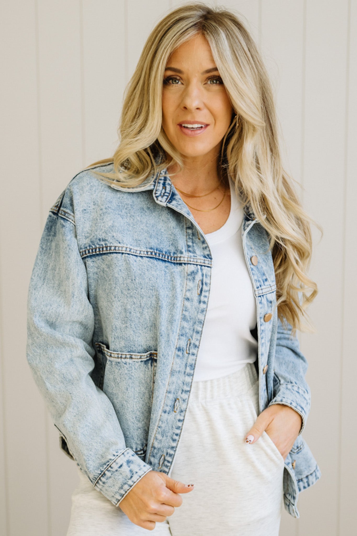 Woman wearing a light blue denim jacket over a white outfit against a neutral background