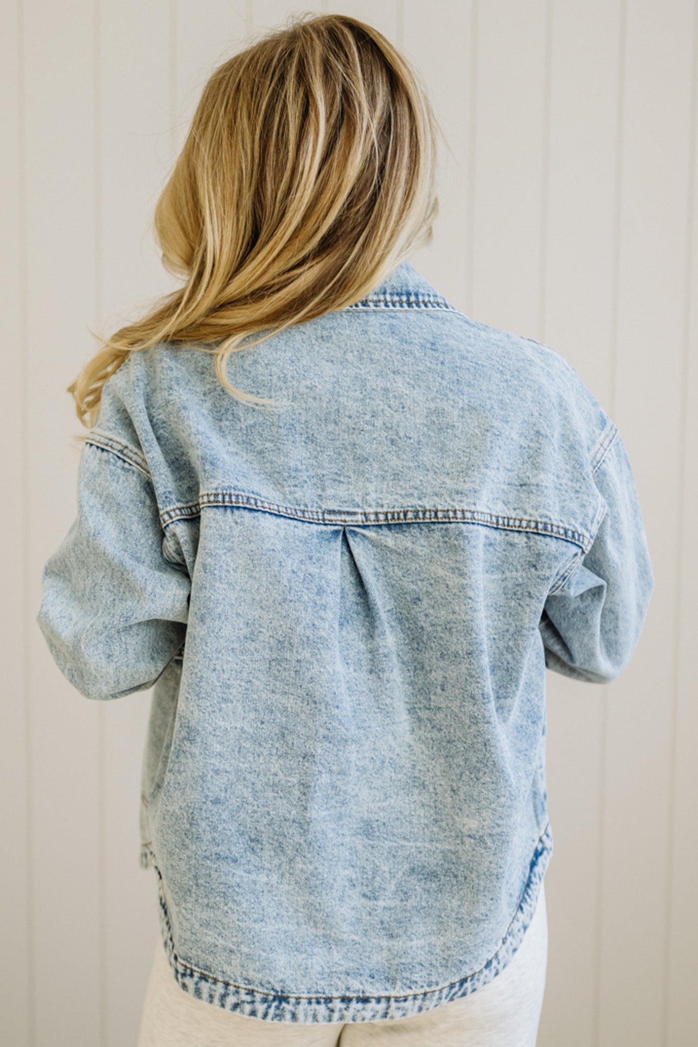 Person wearing a light blue denim jacket with a neutral background