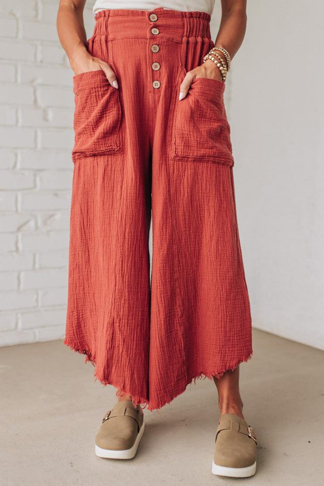 Person wearing red wide-leg pants with button details against a white brick wall.