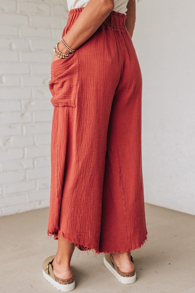 Person wearing rust-colored wide-leg pants against a white brick wall.