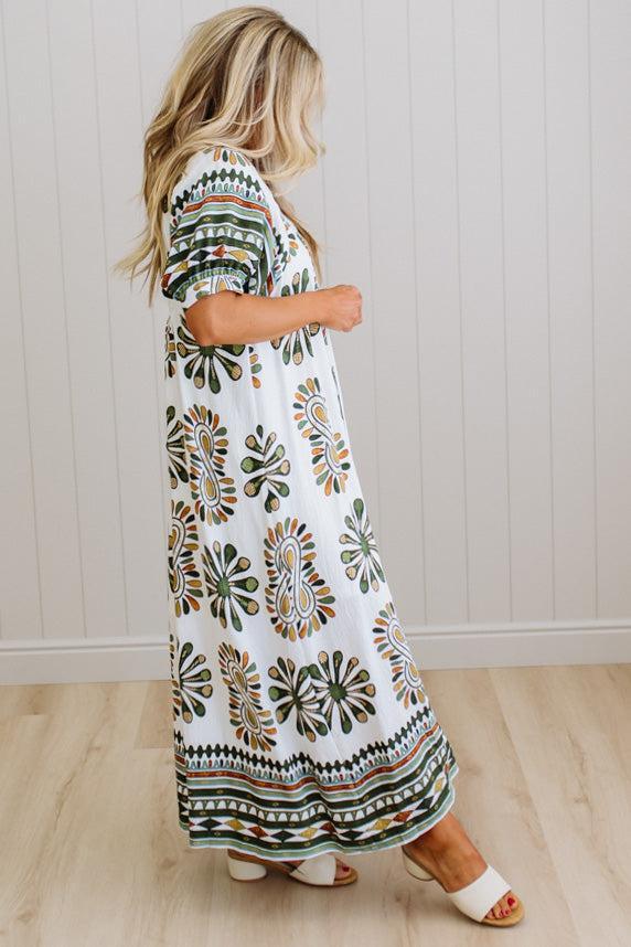 Woman wearing a patterned dress standing against a white paneled wall.