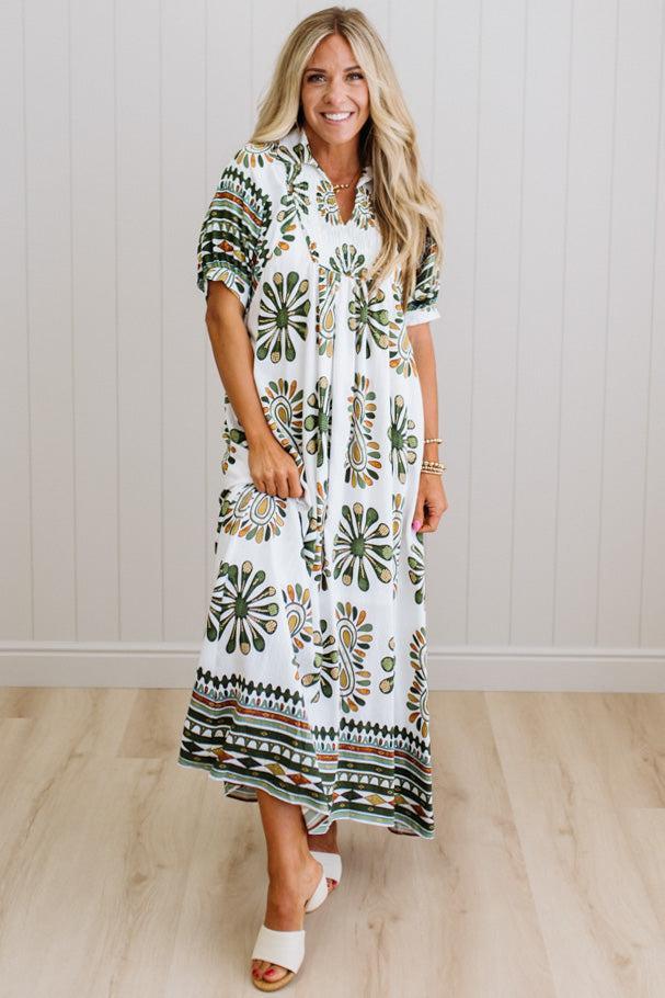 Woman wearing a long, patterned dress standing against a white wall.