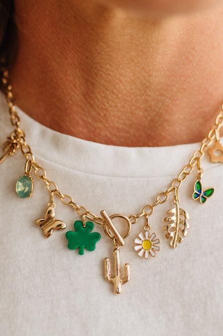Gold necklace with various charms including a clover, butterfly, and cactus on a white background.
