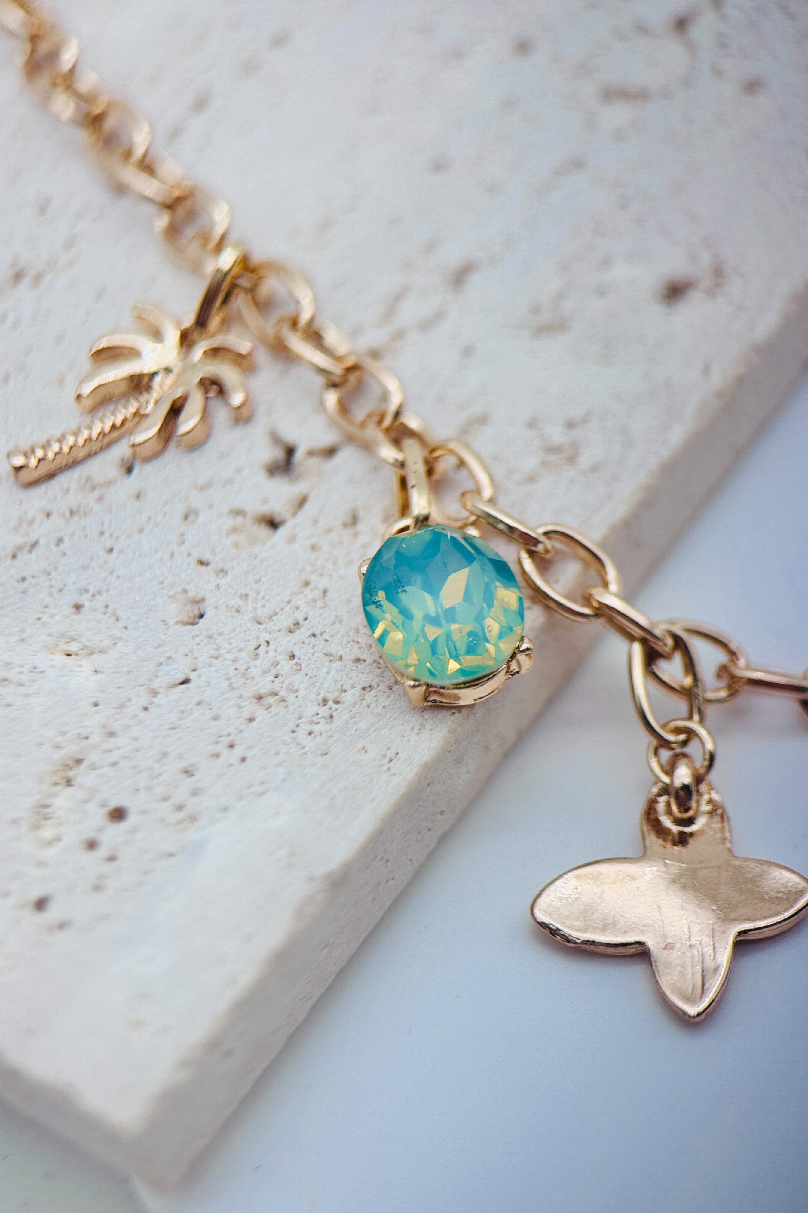 Gold necklace with a geen-blue gemstone and whale charm on a light stone surface