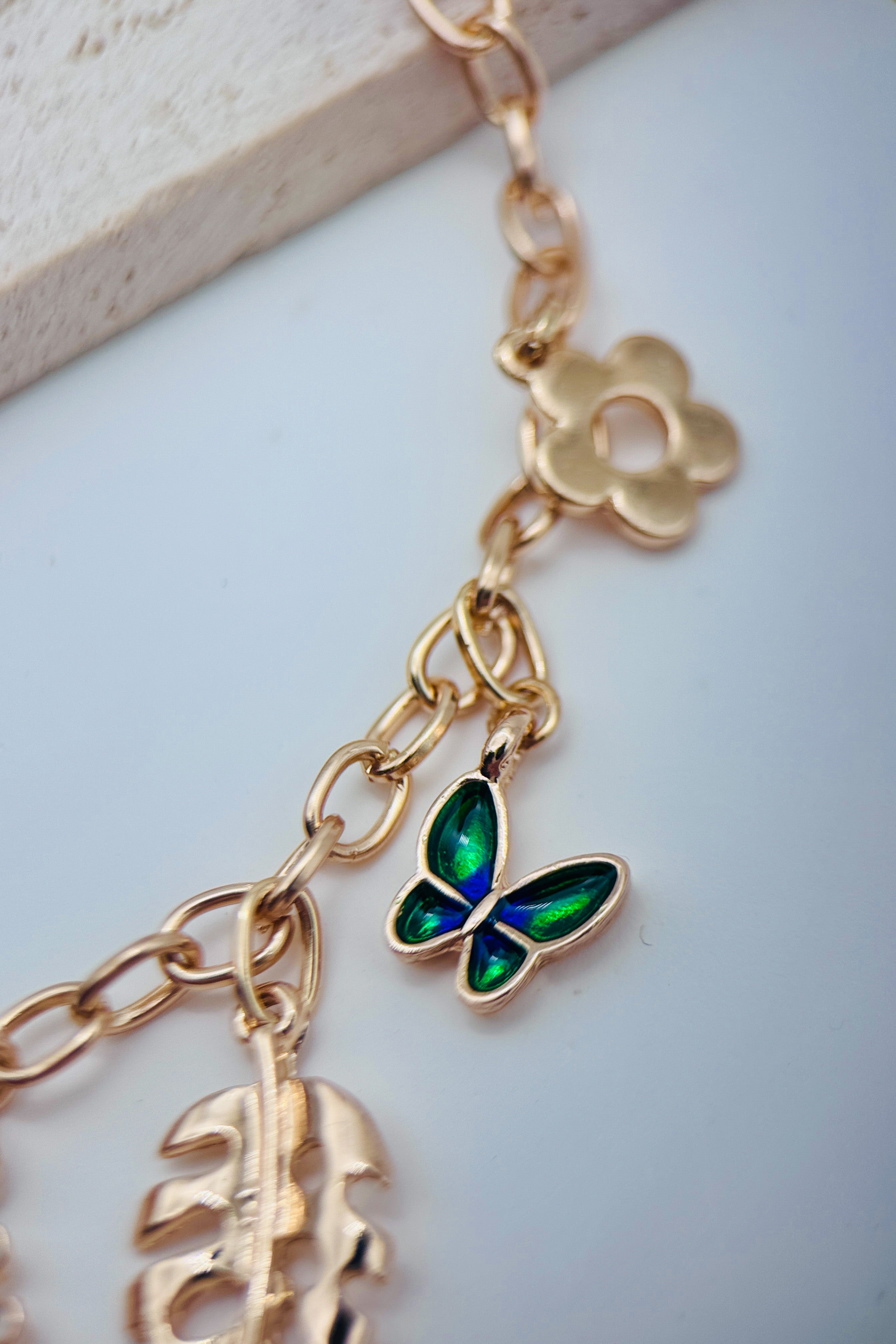Gold necklace with butterfly and leaf charms on a light background