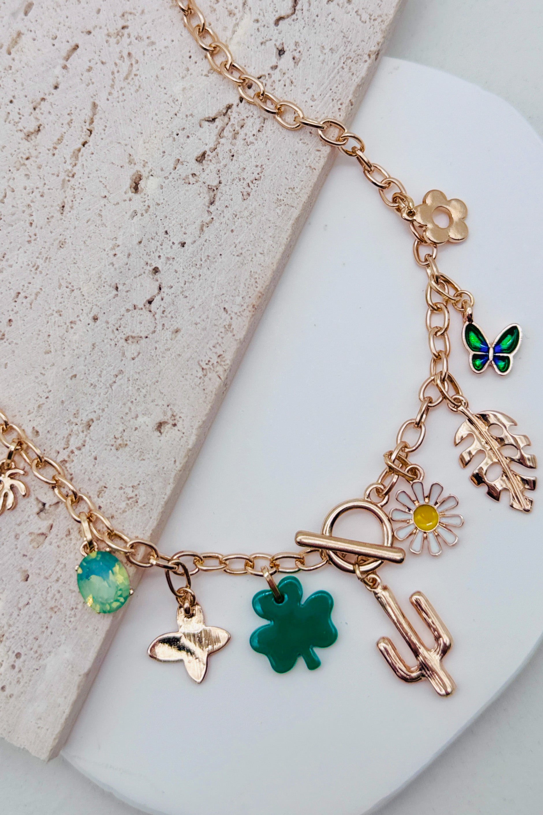 Gold necklace with various charms including a butterfly, flower, and cactus on a light background