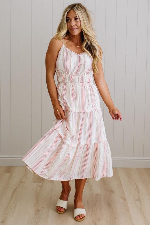 Woman wearing a white dress with red stripes against a light wooden panel background