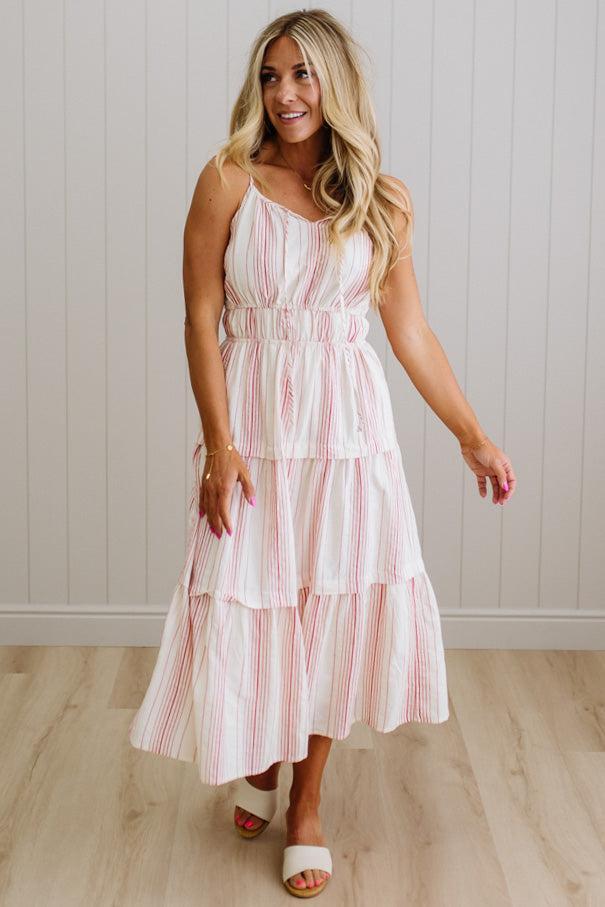 Woman wearing a white dress with red stripes in a room with wooden flooring and a white wall.