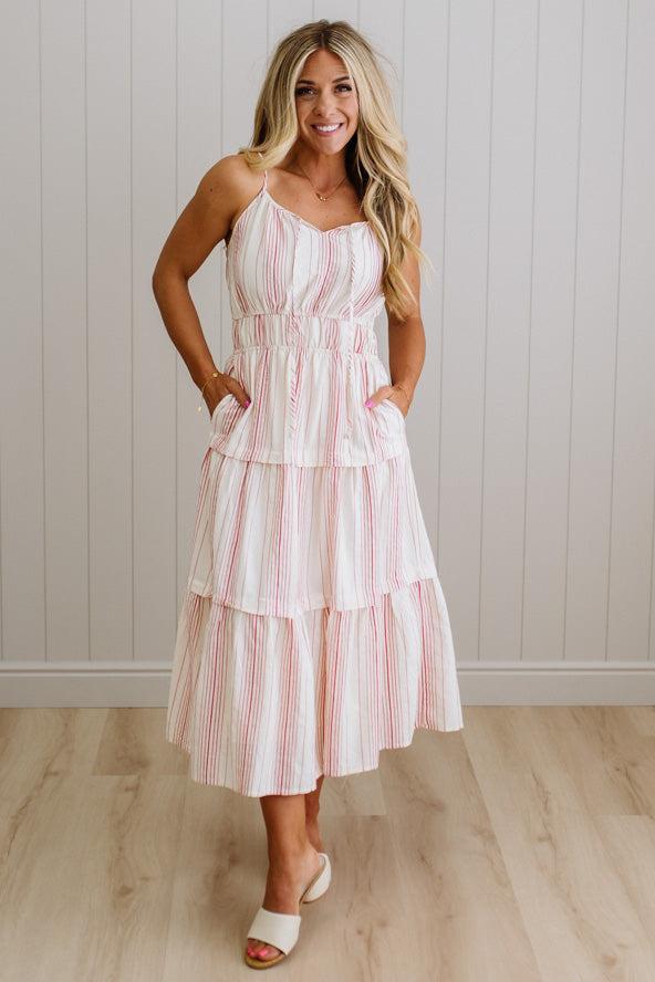 Woman wearing a striped dress standing against a white paneled wall.