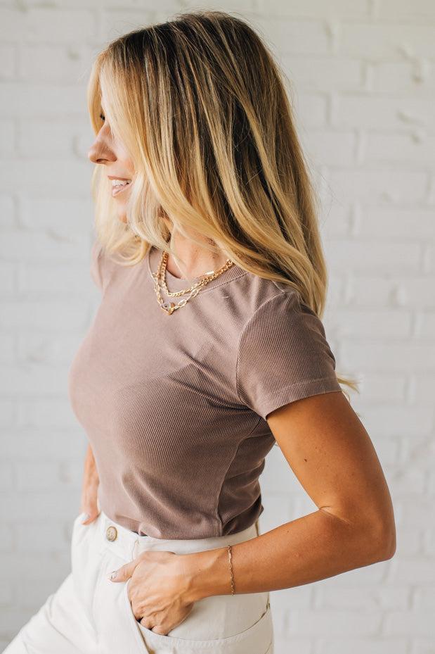 Woman wearing a brown t-shirt and white pants against a light gray background