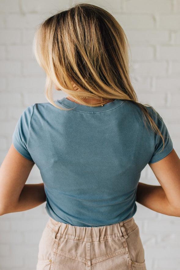 Person wearing a blue t-shirt and beige pants against a white brick wall.