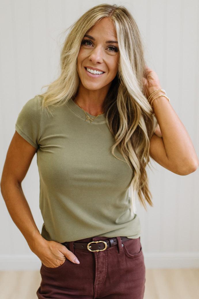 Woman wearing a green t-shirt and brown jeans against a neutral background