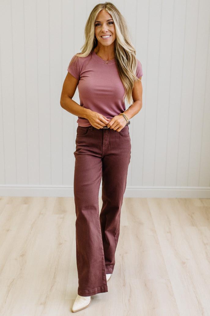 Woman wearing a pink t-shirt and brown jeans against a neutral background