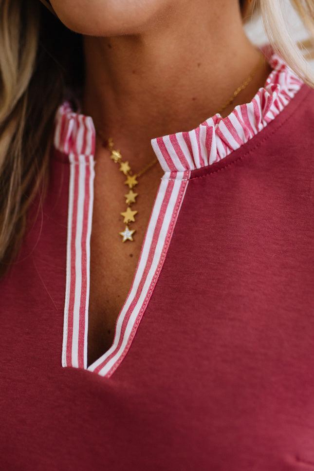 Close-up of a person wearing a red top with white trim and gold star necklaces.