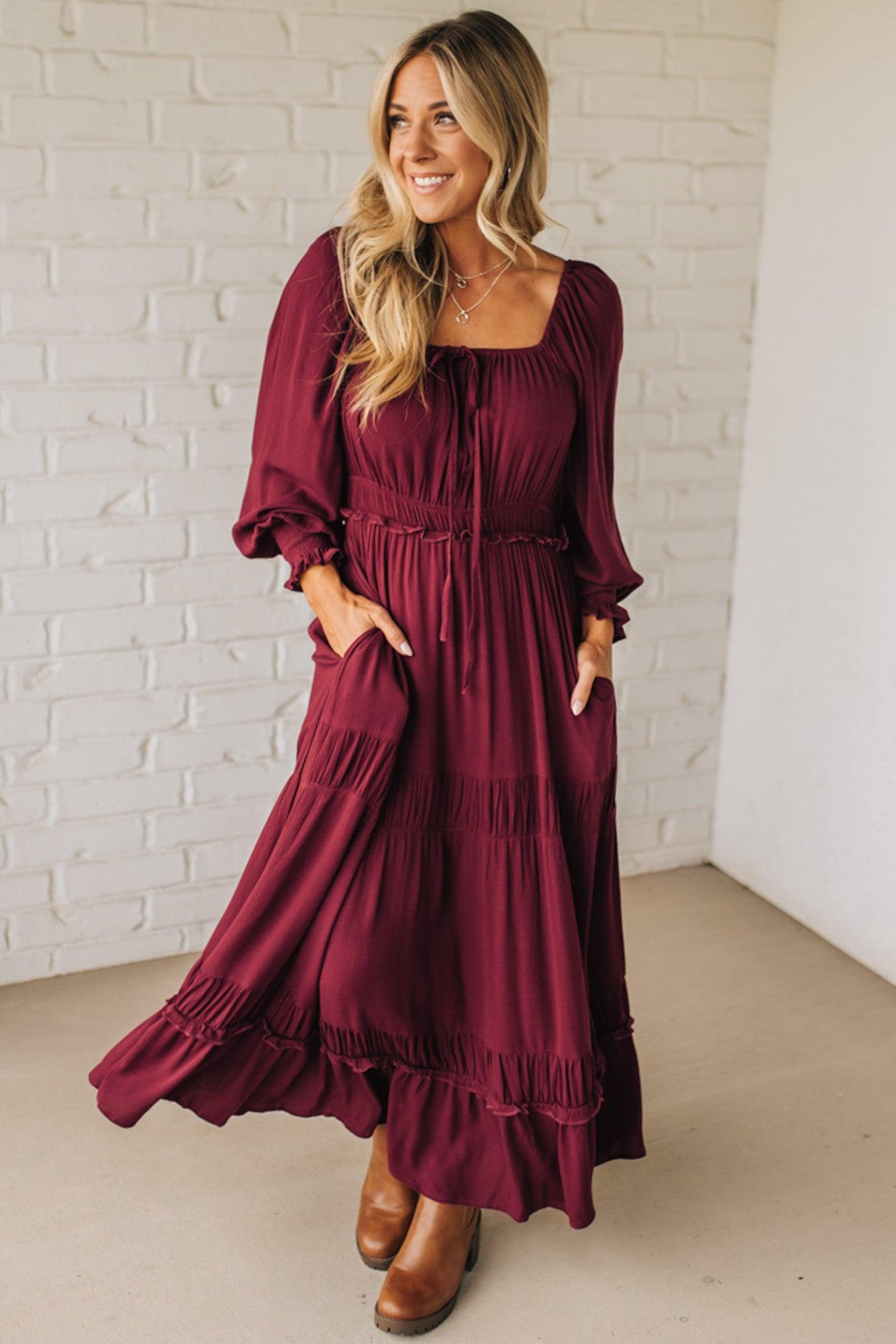 Woman wearing a burgundy dress with long sleeves and a white brick wall background