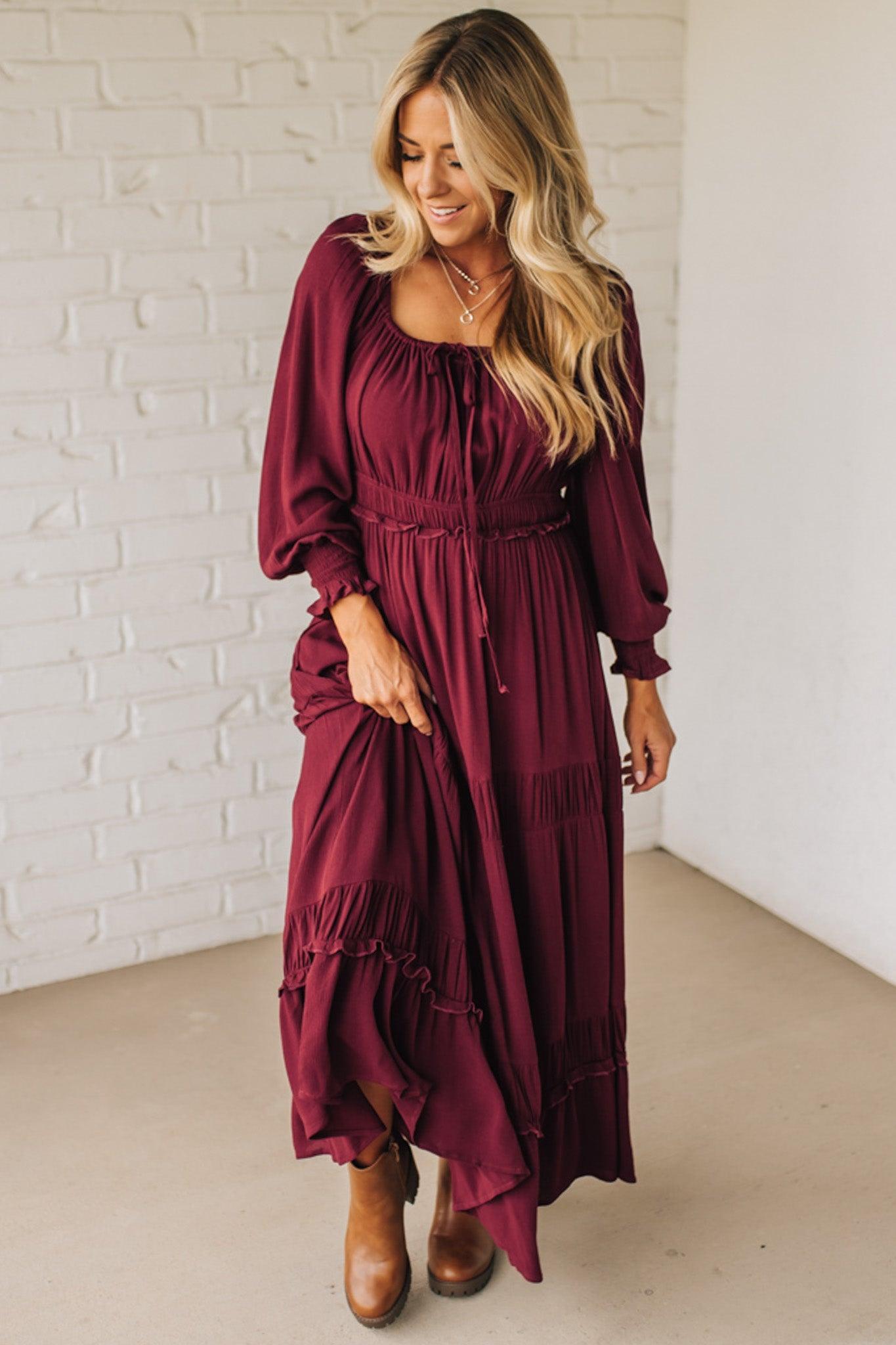 Woman wearing a burgundy dress with long sleeves and a white brick wall background