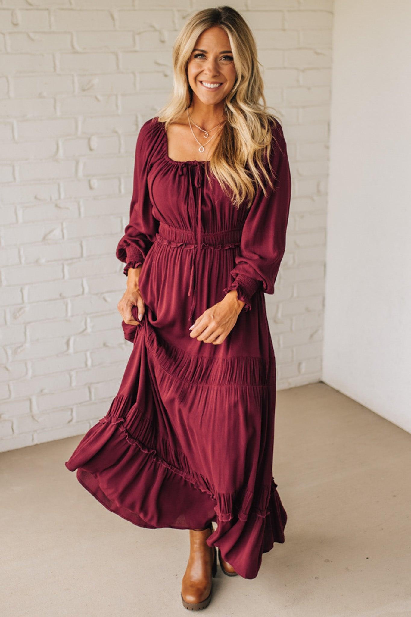 Woman wearing a burgundy dress standing against a white brick wall.