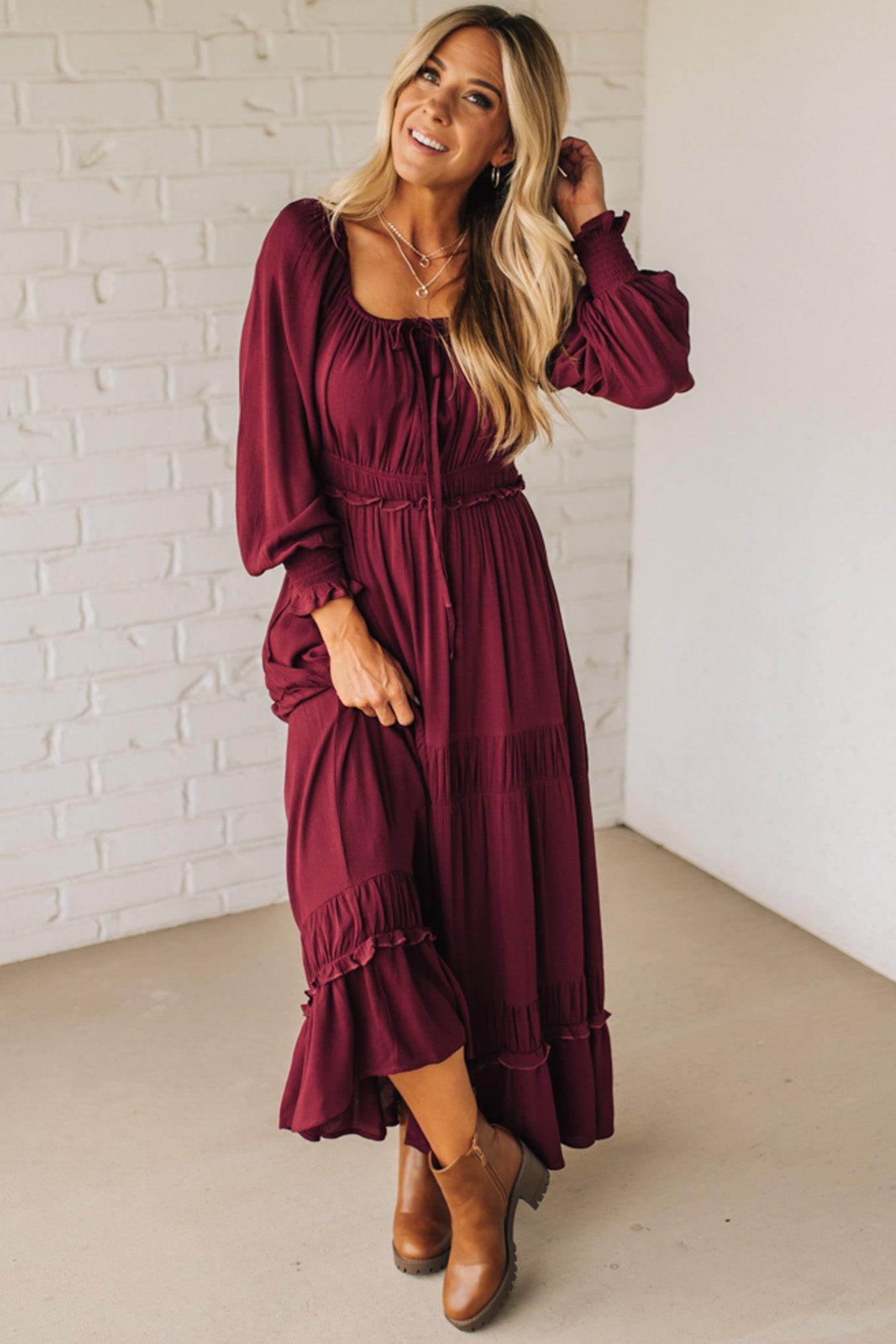 Woman wearing a burgundy dress with long sleeves and a white brick wall background