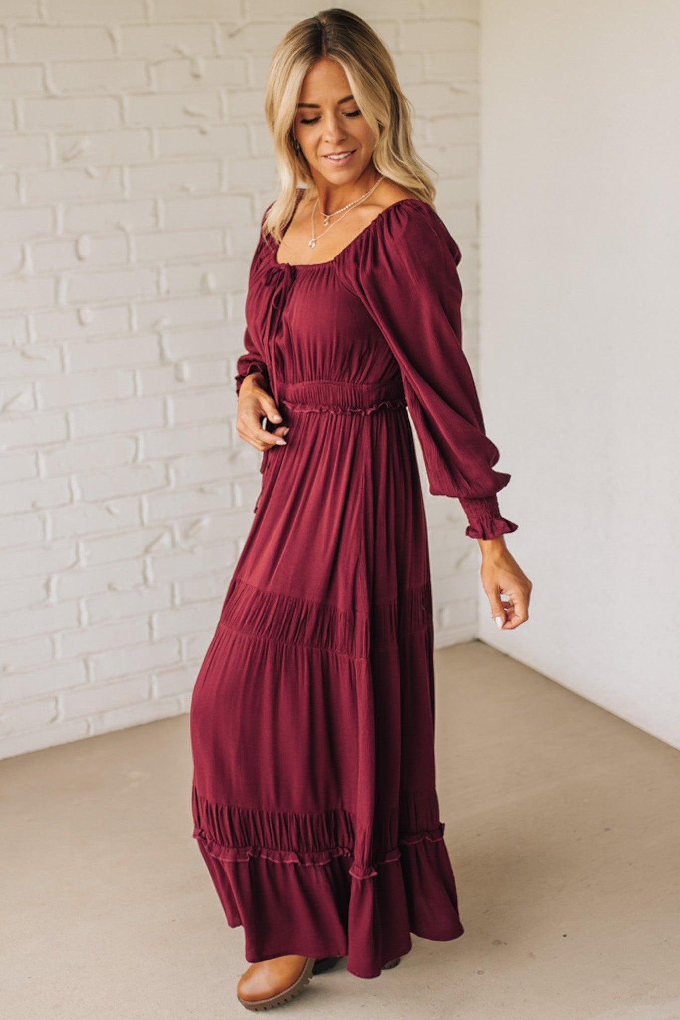 Woman wearing a burgundy dress against a white brick wall.