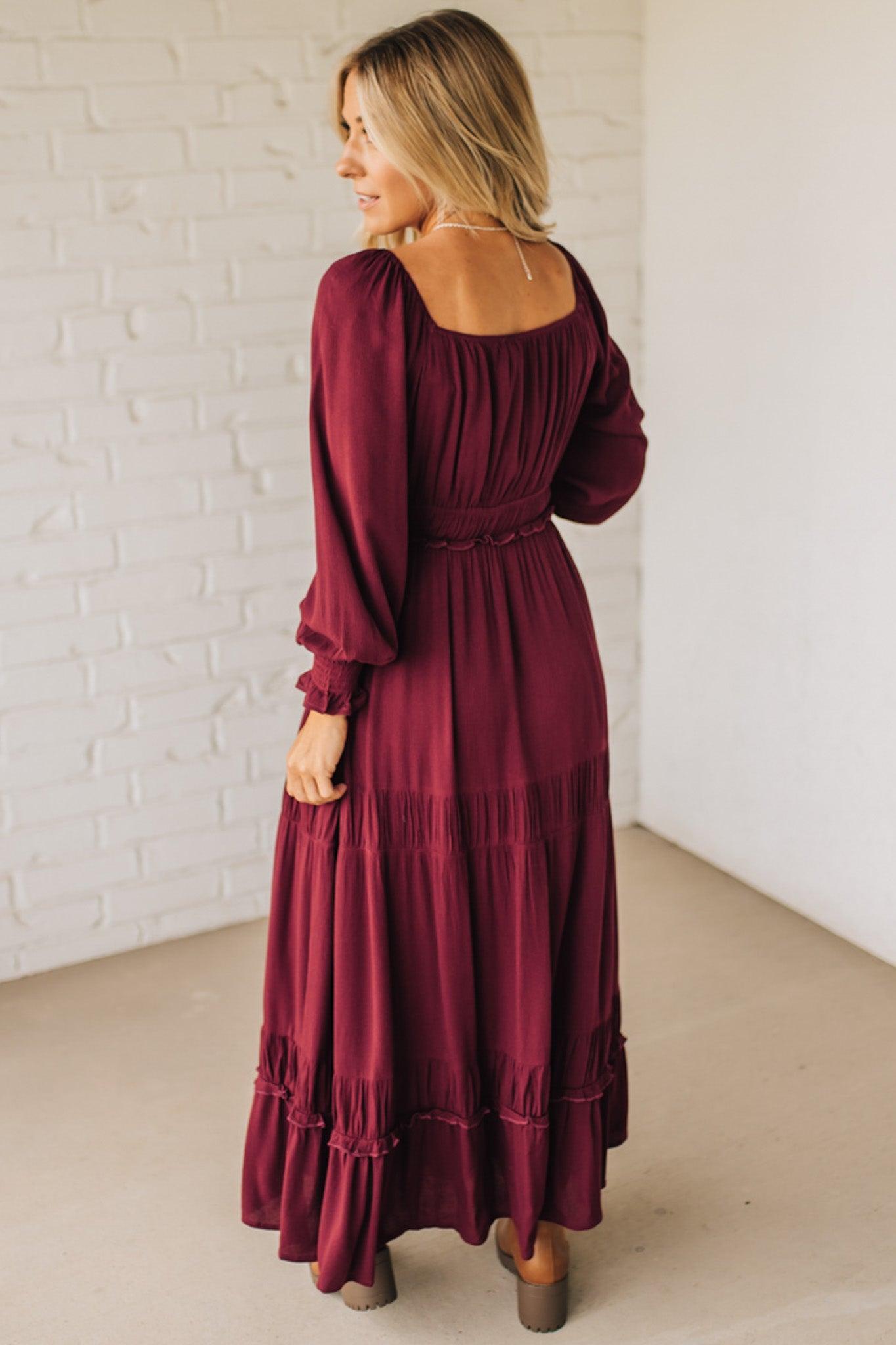 Woman wearing a burgundy dress with long sleeves in a minimal indoor setting.