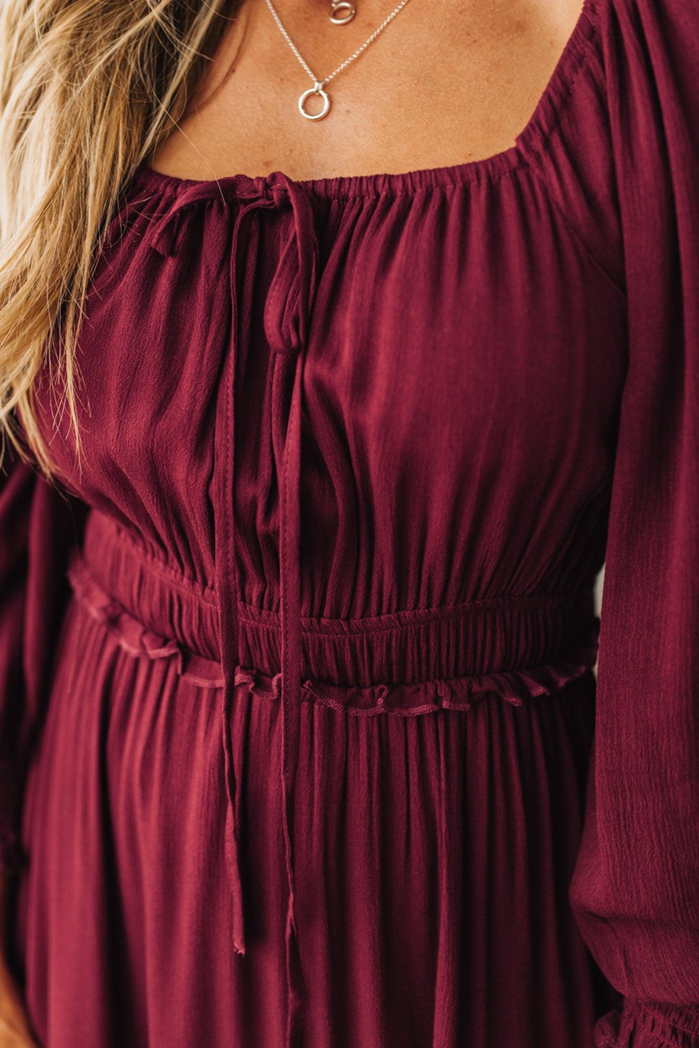 Close-up of a burgundy dress with long sleeves and a necklace.