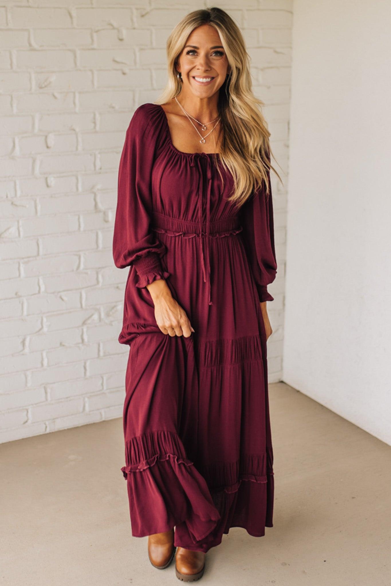 Woman wearing a burgundy dress standing against a white brick wall.