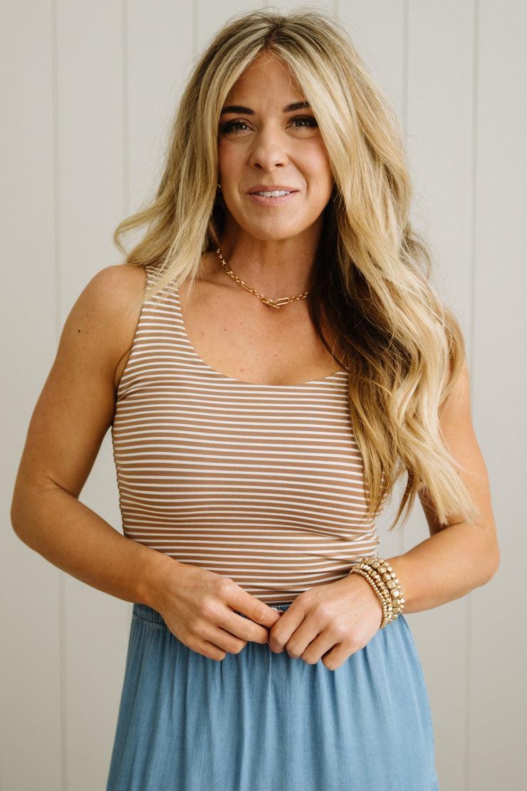 Woman wearing a striped tank top and blue skirt against a neutral background