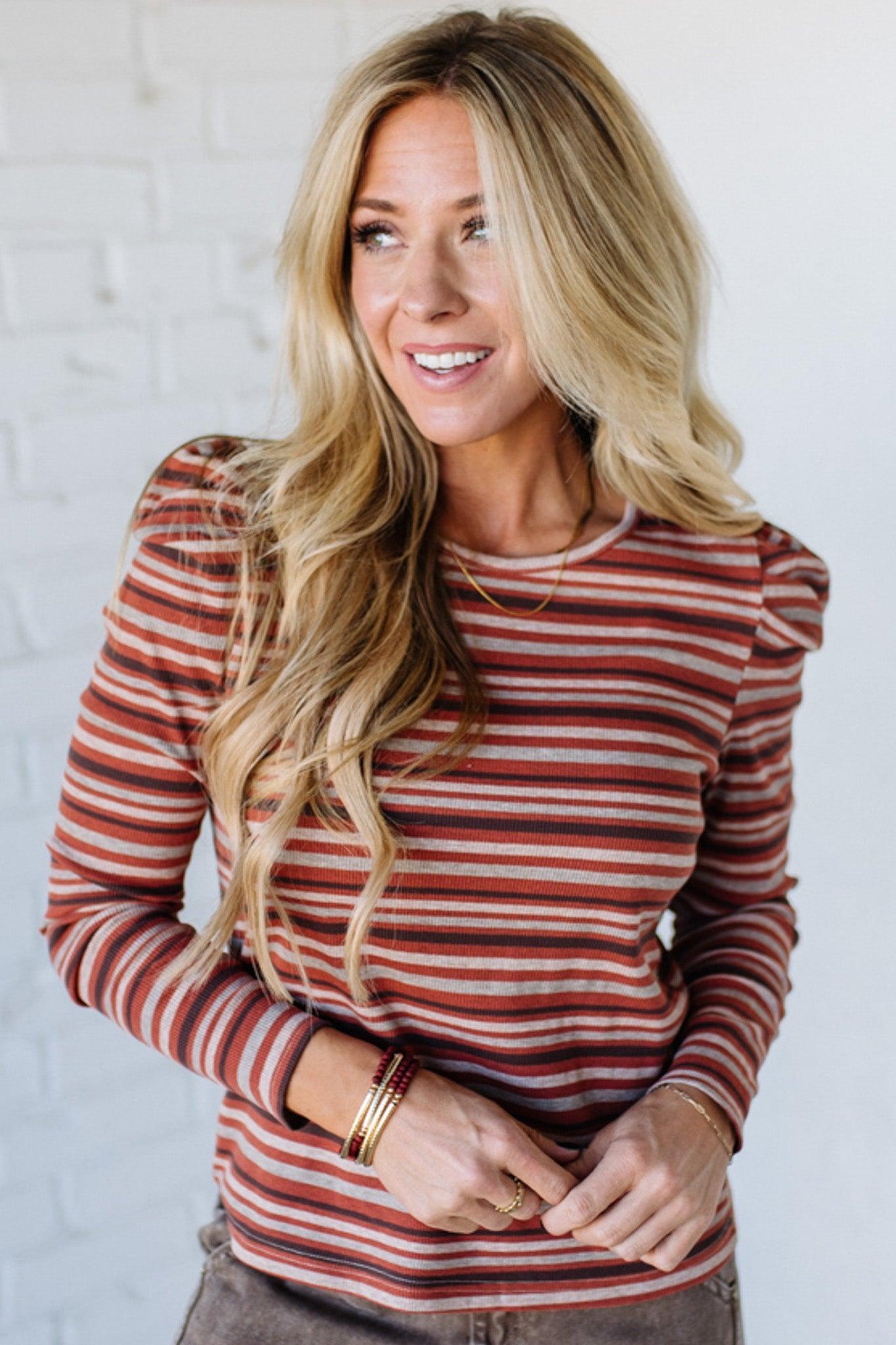 Woman wearing a striped long-sleeve top against a white brick wall.