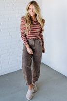 Woman wearing a striped shirt and brown pants against a white brick wall.