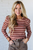 Woman wearing a striped long-sleeve top against a white brick wall